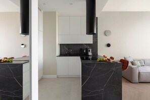 Una cocina moderna con encimera de mármol negro, armarios blancos y un sofá gris en la sala de estar.