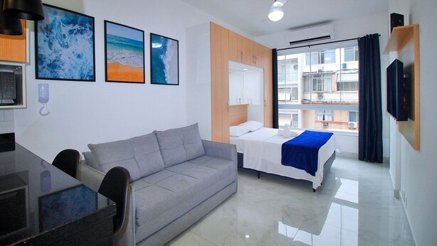 Ein Hotelzimmer mit einer Couch, einem Bett, einem Schreibtisch und einem großen Fenster mit Blick auf Gebäude.
