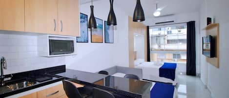 Une cuisine moderne avec un îlot central, des tabourets de bar noirs et une table à manger. Un micro-ondes est installé au-dessus de l’îlot, et la cuisine est dotée d’armoires en bois.