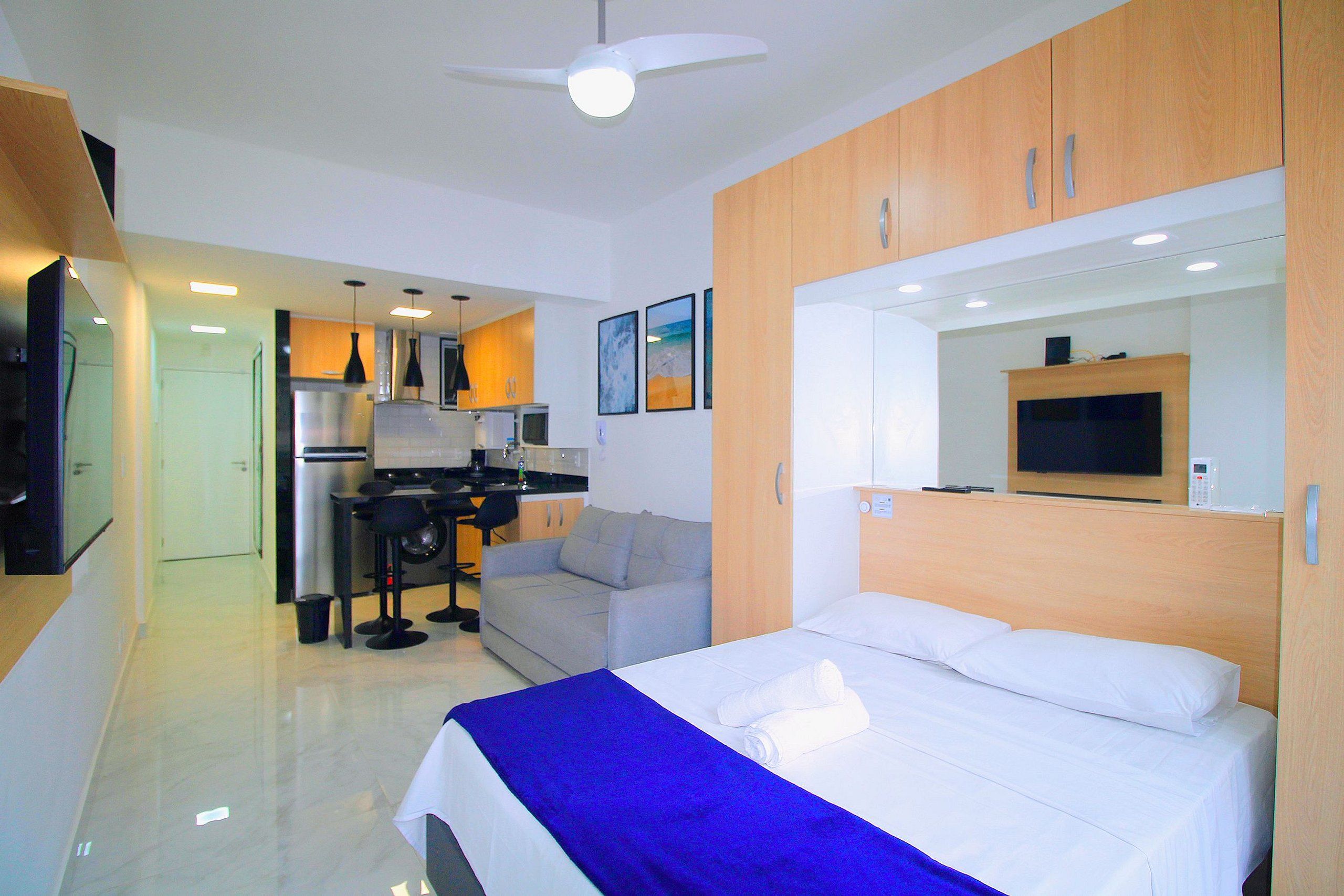 A compact hotel room with a bed, a kitchenette, a seating area, and a large mirror.