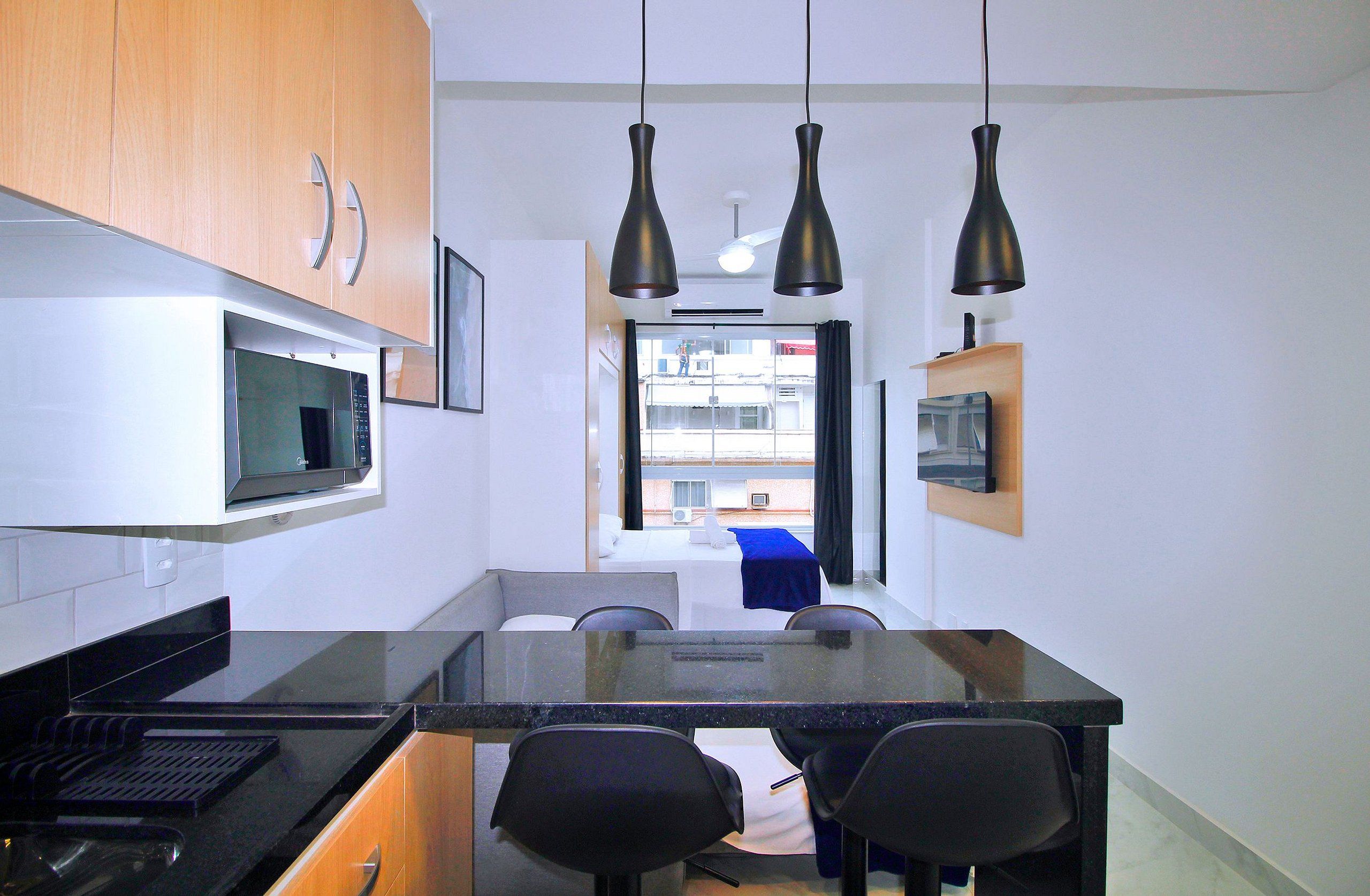 A compact kitchen with a microwave, a dining table with chairs, and pendant lights.