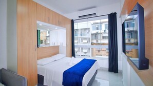 Ein Hotelzimmer mit einem Bett, einem Schreibtisch, einem Spiegel und einem Fenster mit Blick auf Gebäude.