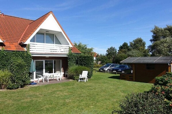 A two-story house with a sloped roof, a balcony, and a covered patio area with outdoor furniture. - Holiday apartment Maike Duhnen (Cuxhaven - Duhnen)