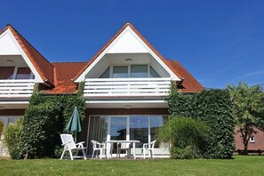 A two-story building with a red-tiled roof, a balcony with white railings, and a patio area with outdoor furniture. - Holiday apartment Maike Duhnen (Cuxhaven - Duhnen)