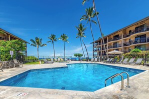 A swimming pool with lounge chairs and palm trees, surrounded by a building with balconies. - Kona Makai 4-106: No Stairs, 2 Bedroom Unit with Wrap Around Lanai & Ac (Kailua Kona)