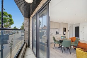 A modern apartment with a balcony overlooking a street, a kitchen with contemporary appliances, and a dining area with green and orange chairs. - Balcony Studio in Northfields - Apt 1 (London)