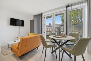 A modern living room with a sofa, chairs, a TV, and a dining table. - Balcony Studio in Northfields - Apt 1 (London)