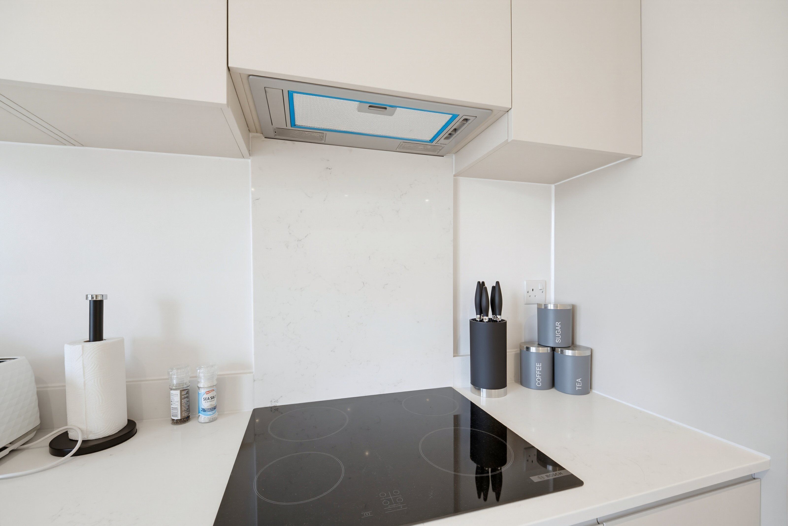 Una cocina moderna con una placa de inducción negra, horno integrado y extractor de acero inoxidable.