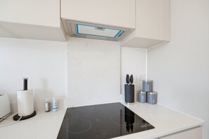 A modern kitchen with a black induction cooktop, a built-in oven, and a stainless steel range hood. - Balcony Studio in Northfields - Apt 1 (London)