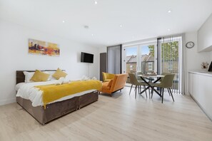 A modern bedroom with a bed, a television, and a dining area with chairs and a table. - Balcony Studio in Northfields - Apt 1 (London)