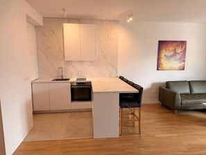 A modern kitchen with marble countertops, a built-in oven, and a dining area with a wooden table and chairs. - Luxe Residence, 2BR, Skopje Central, Riverside, Vodno View, AC (Skopje)