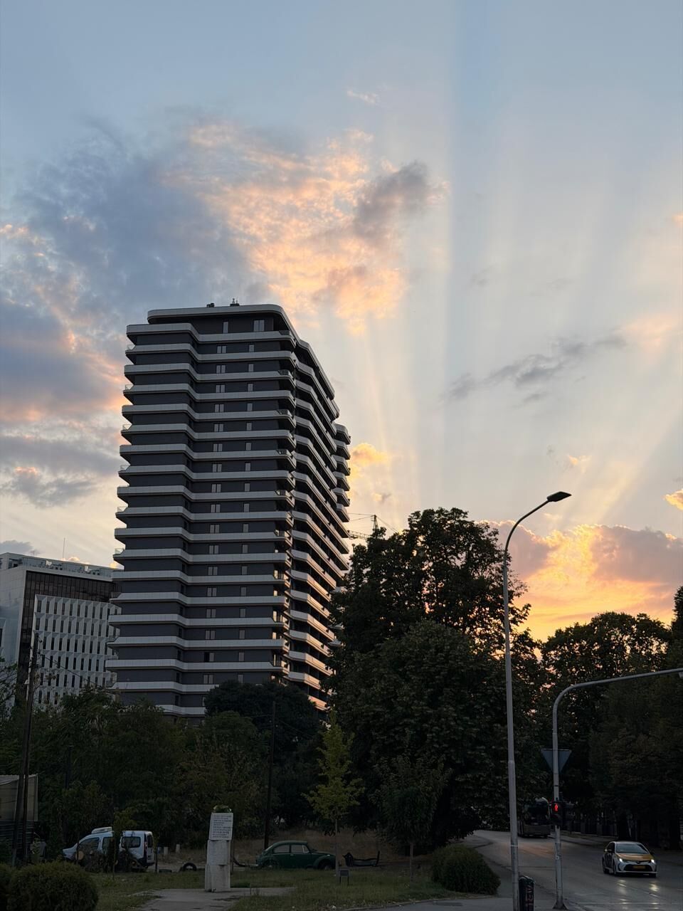 Korkea kerrostalo, jossa on moderni arkkitehtoninen ilme, ja sen ympärillä on vehreää kasvillisuutta ja avoin, kirkas taivas.