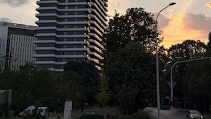 Een hoog gebouw met een modern architectonisch ontwerp, omgeven door groen en een heldere lucht.