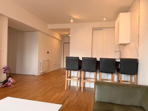 A modern living room with a wooden floor, a green sofa, and a dining area with four chairs. - Luxe Residence, 2BR, Skopje Central, Riverside, Vodno View, AC (Skopje)