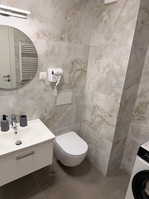 Ein Badezimmer mit einem weißen Waschbecken, einer Toilette und einem an der Wand befestigten Föhn.