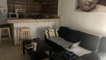 En stue med sofa, sofabord, en bærbar computer og et lille bord med en fjernbetjening.