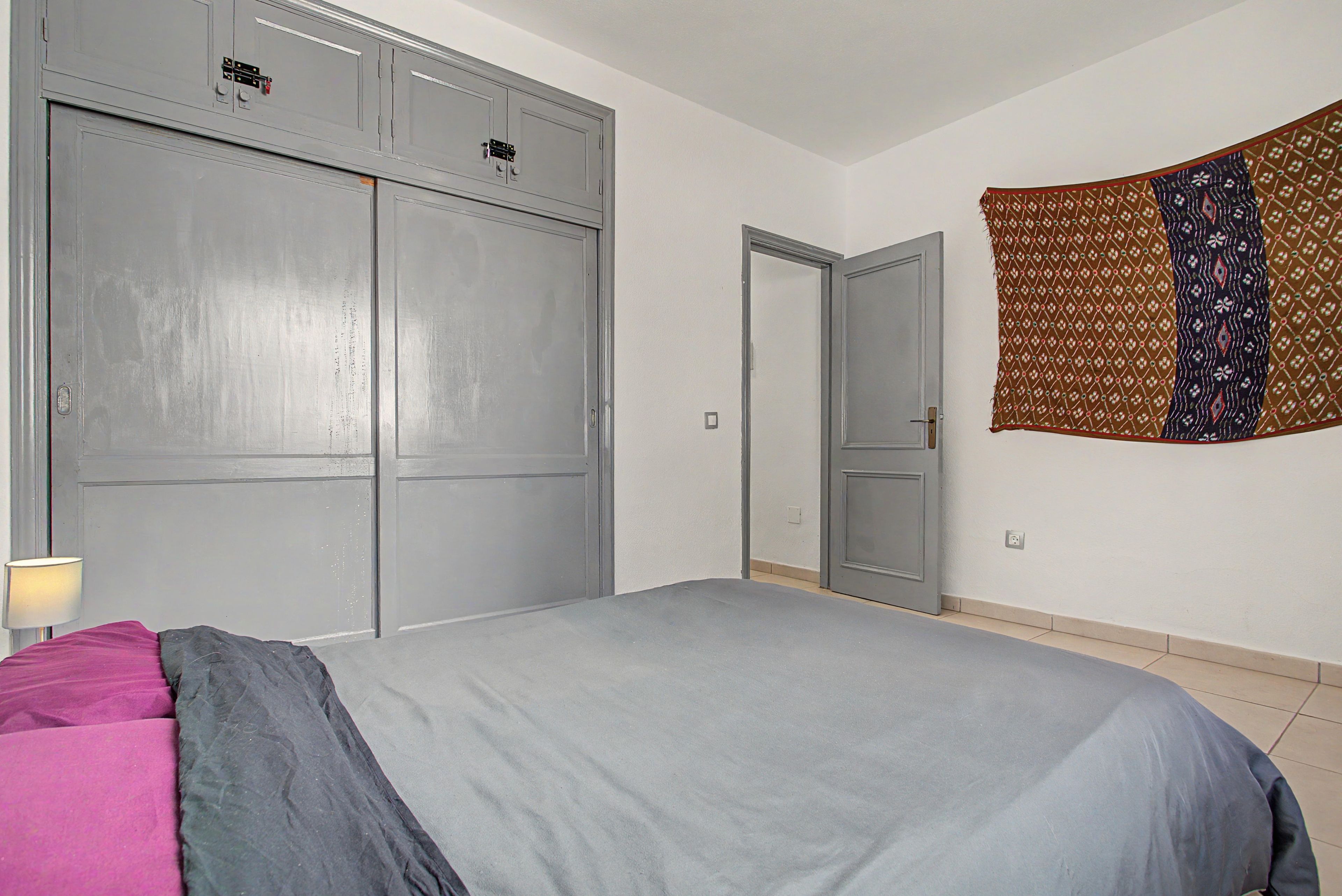 Een slaapkamer met een bed, een kledingkast, een deur en een wanddecoratie.