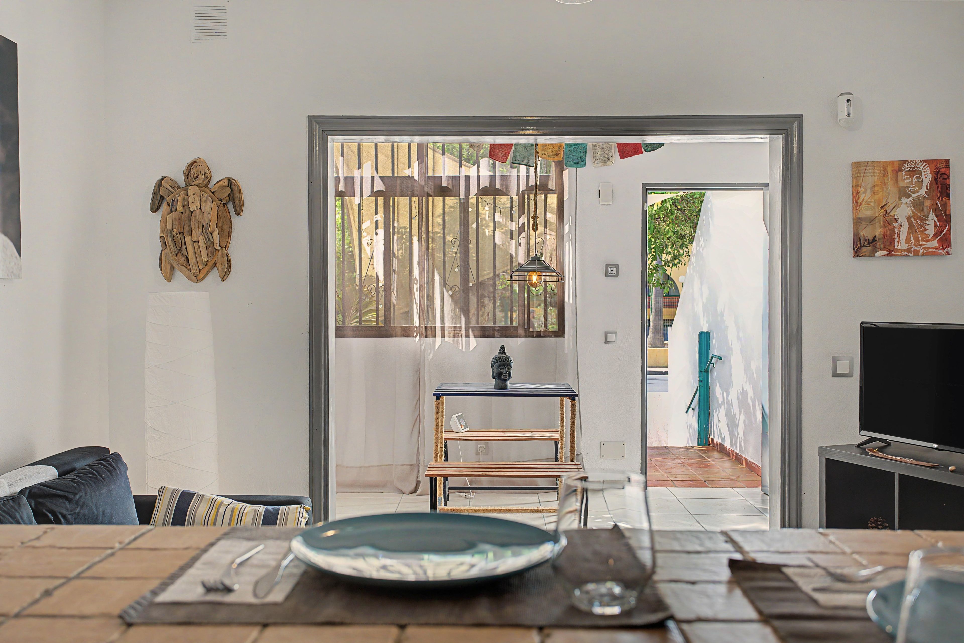 A modern living room with a dining area, a sofa, a TV, and a view through a doorway.