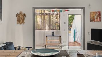A modern living room with a dining area, a sofa, a TV, and a view through a doorway.