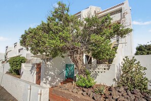Un edificio residencial con un árbol en primer plano, una reja y un pequeño jardín con cactus.