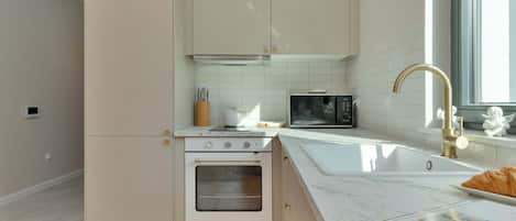 Una cocina moderna con armarios blancos, horno empotrado, microondas y un amplio ventanal que proporciona luz natural.