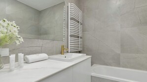Un bagno moderno con un lavandino bianco, un rubinetto dorato, un asciugamano bianco e una vasca da bagno bianca.