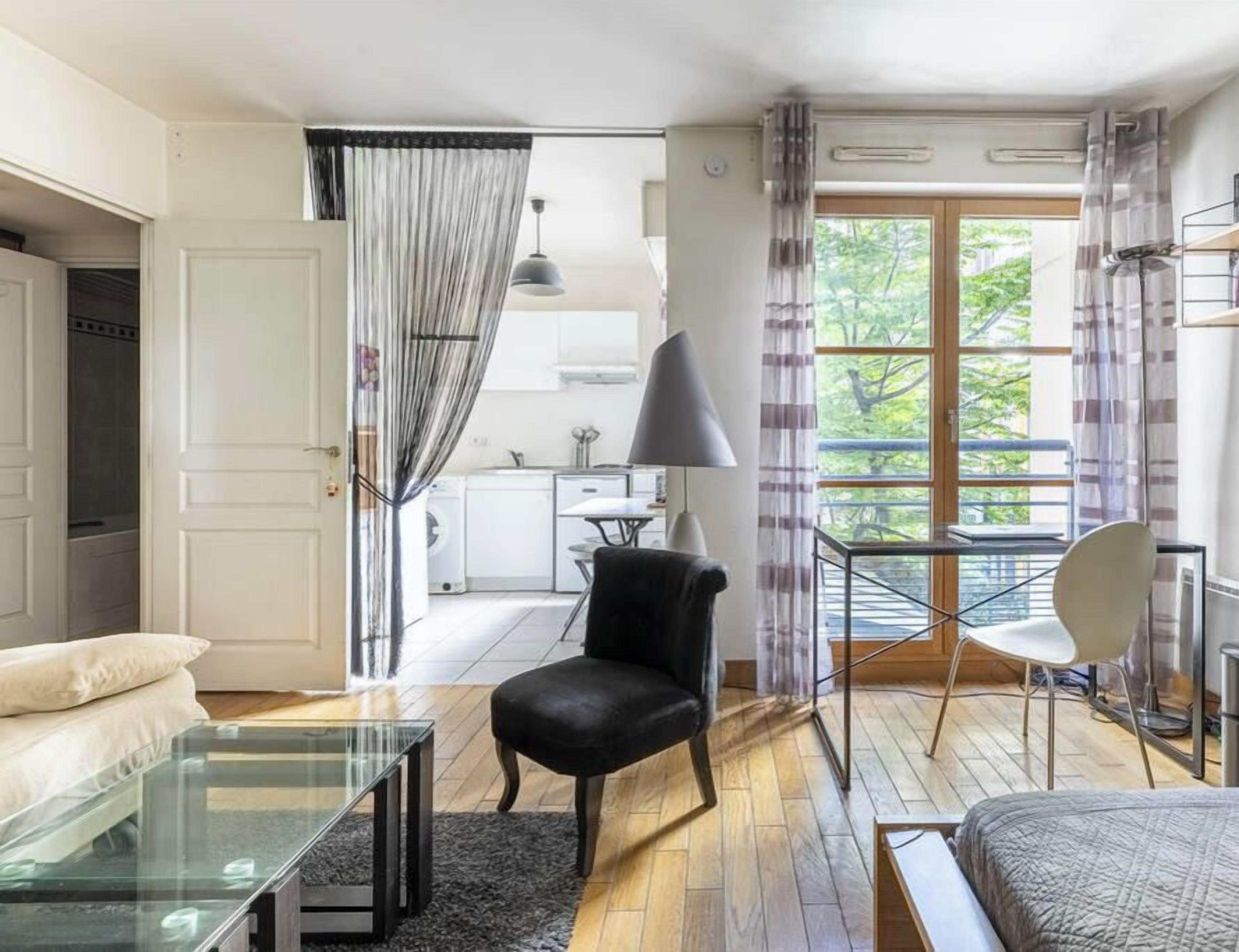 A modern bedroom with a glass table, a black chair, a bed, and a view of a balcony.