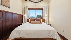 A hotel room with a large bed, wooden paneling, a circular ceiling light, a window with curtains, and a wall-mounted painting. - Morehead City House - Loft - One bedroom suite with full kitchen and living area (Morehead City)