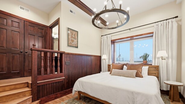A bedroom with a large bed, a wooden staircase, a window with curtains, and a chandelier. - Morehead City House - Loft - One bedroom suite with full kitchen and living area (Morehead City)