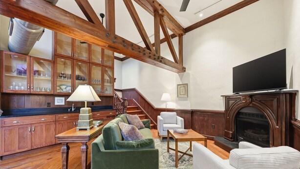 A spacious living room with a fireplace, wooden beams, a television, and a dining area with a table and chairs.