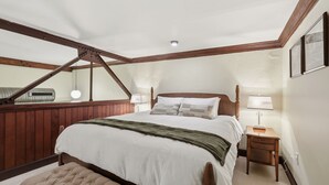 A bedroom with a large bed, a wooden headboard, a nightstand, a lamp, a mirror, and a radiator.
