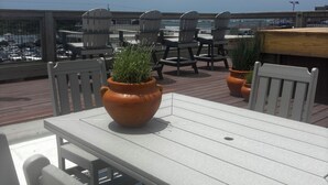 A rooftop terrace with a table and chairs, potted plants, and a view of the cityscape.