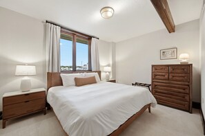 Une chambre à coucher avec un grand lit, deux tables de chevet avec des lampes, une commode en bois et une fenêtre avec des rideaux.
