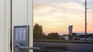 A door with a numeric keypad lock and a view of a sunset through a window.