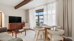 A modern living room with a flat-screen TV, wooden cabinet, and a dining area with chairs and a table.