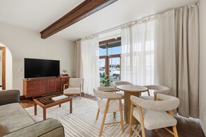 A modern living room with a flat-screen TV, wooden cabinet, and a dining area with chairs and a table.