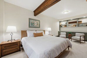 Une chambre d’hôtel avec un grand lit, deux tables de chevet avec des lampes, une chaise, un bureau avec un miroir et une bibliothèque.