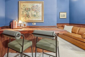 Una habitación con pared azul, un mostrador de recepción de madera, dos sillas verdes, un sofá de cuero marrón y un cuadro enmarcado.