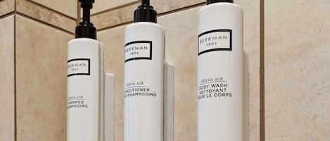 Três frascos de Beckman 1802 com produtos de banho e shampoo para purificação da pele sobre uma parede de azulejos.