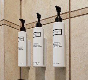 Trois bouteilles de gel douche et de shampoing Beckman 1802, parfum « air frais », sont posées sur un mur carrelé.