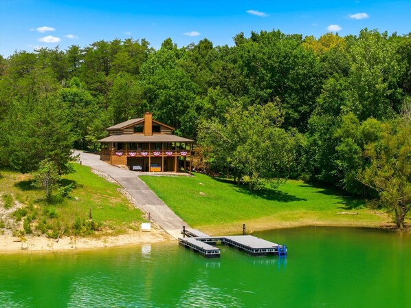 A lodge with a covered porch, a dock, and a lake. - Douglas Lakefront Cabin, Boat Ramp, Private Dock, Hot Tub! (Sevierville)