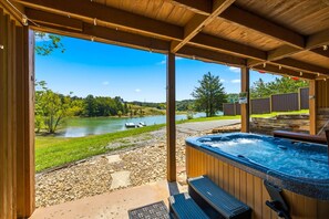Un espace extérieur abrité comprenant un jacuzzi, une vue sur un lac et une terrasse en bois.