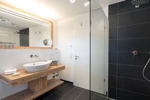 A modern bathroom with a wooden vanity, a large mirror, a white sink, and a glass-enclosed shower area. - Holiday apartment in Oberstdorf with sauna (Oberstdorf)