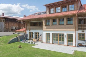 A two-story house with a sloped roof, large windows, and a paved patio area. - Holiday apartment in Oberstdorf with sauna (Oberstdorf)