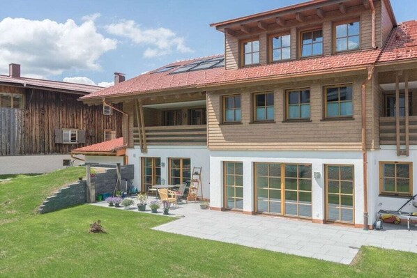 A two-story house with a sloped roof, large windows, and a paved patio area. - Holiday apartment in Oberstdorf with sauna (Oberstdorf)