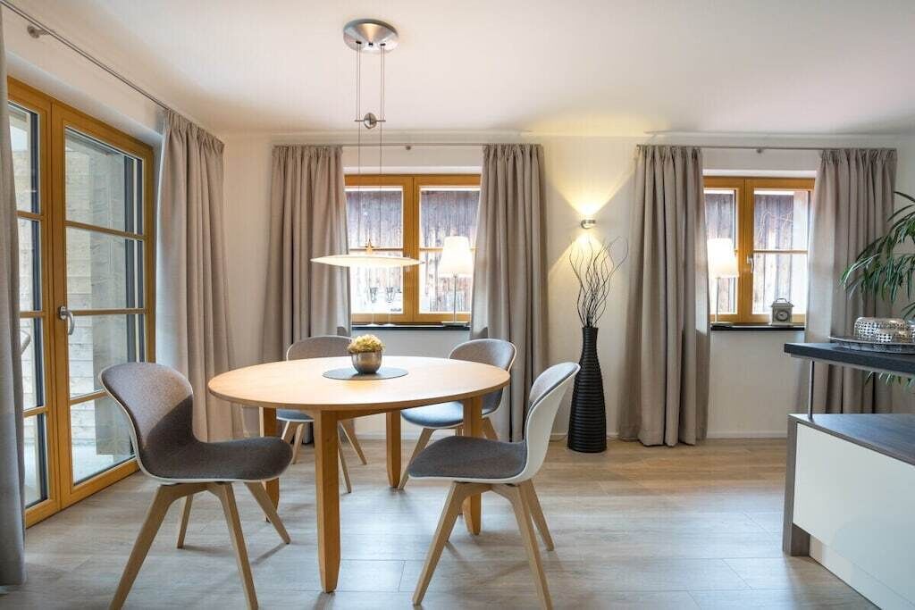 Ein moderner Essbereich mit einem runden Tisch, vier Stühlen und einer Blumenvase.