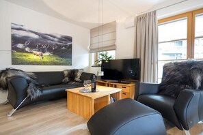 A modern living room with a sofa, a coffee table, a television, and a large window with curtains. - Holiday apartment in Oberstdorf with sauna (Oberstdorf)