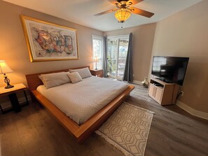 A bedroom with a bed, a television, a ceiling fan, a window, and a painting on the wall. - Coastal Retreat ABC Cottage by the Sea (Seaside)