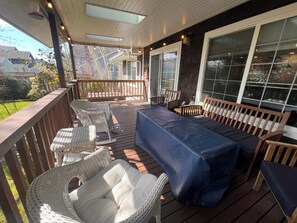 Eine überdachte Terrasse im Freien mit Korbmöbeln, einer blauen gepolsterten Bank und großen Fenstern.