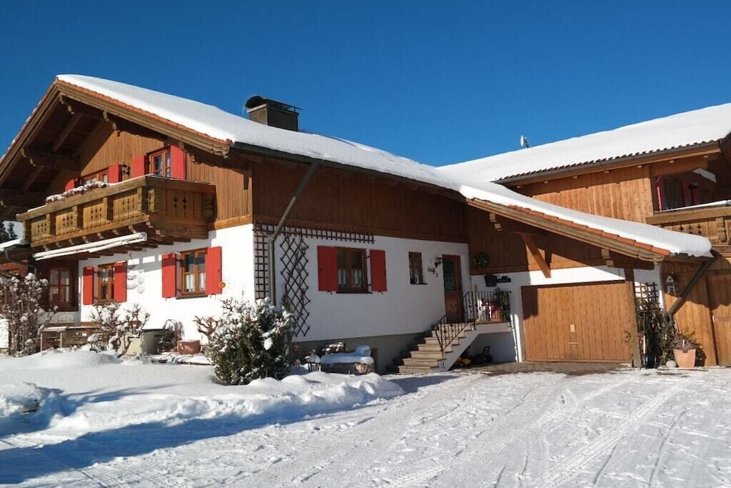 Un chalet en bois doté d’un balcon, d’un escalier menant à l’entrée et d’un toit recouvert de neige.